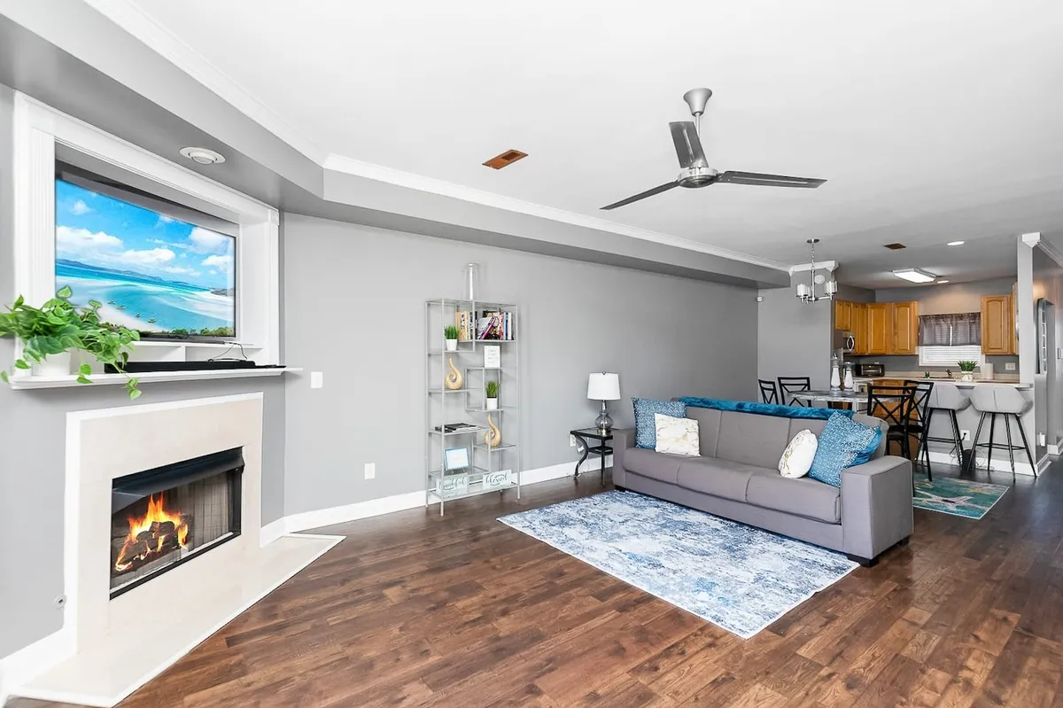 The image showcases a beautifully styled living room with a cozy sofa centered around a glowing fireplace, decorative shelving lining the walls, and a large window offering a serene sunset view. The space exudes warmth and comfort, inviting guests to unwind, read, or entertain friends after a day of exploring Charleston.