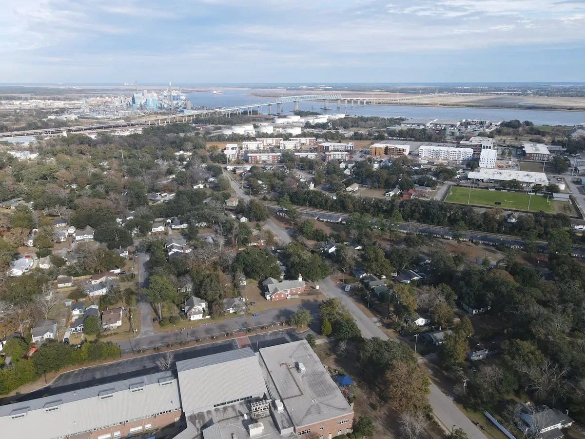 This image features a sweeping view of the river, with a picturesque bridge and the Charleston city skyline visible in the distance. Residential neighborhoods are nestled along the waterfront, blending urban energy with tranquil natural beauty. The scene captures the essence of Downtown Charleston's accessibility and vibrant atmosphere.