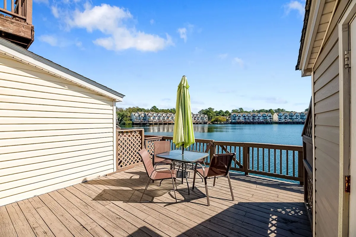 This exterior image features a table with chairs under a yellow umbrella, set on a deck overlooking calm water. The inviting setup suggests outdoor dining or relaxation with scenic lake views, evoking a peaceful family setting after a day of exploration.