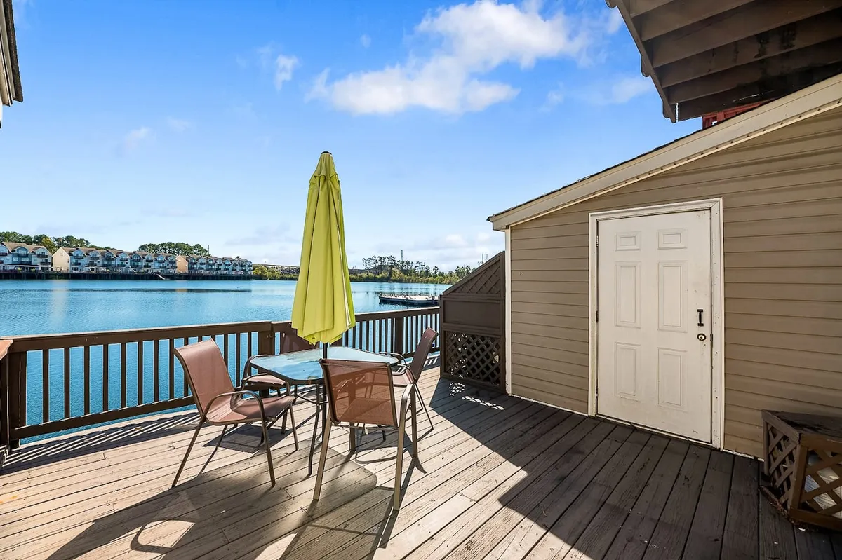 An inviting lakeside patio setup with a table, chairs, and a cheerful yellow umbrella overlooking calm water. The space is perfect for relaxing, dining, or unwinding after a busy day in the city, offering a peaceful retreat that contrasts with the urban excitement of downtown.