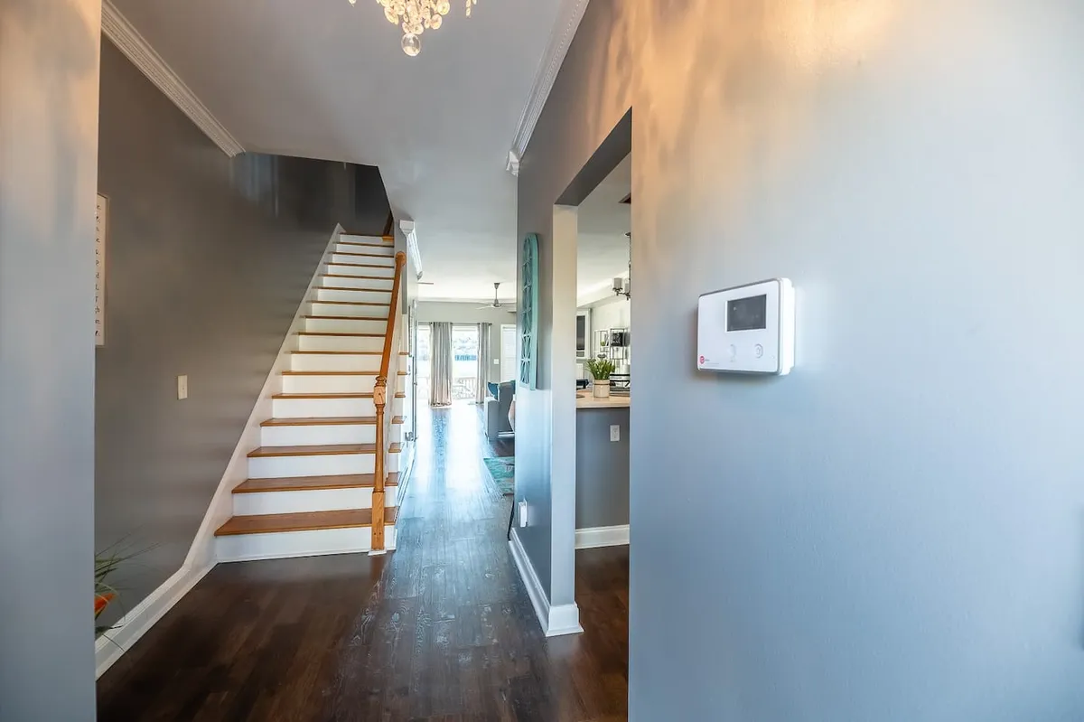This interior image features a staircase with a chandelier overhead and an open doorway, creating a sense of movement and connection between spaces. The warm lighting and inviting layout immediately greet guests, visually representing the transition from entry to the rest of the home.